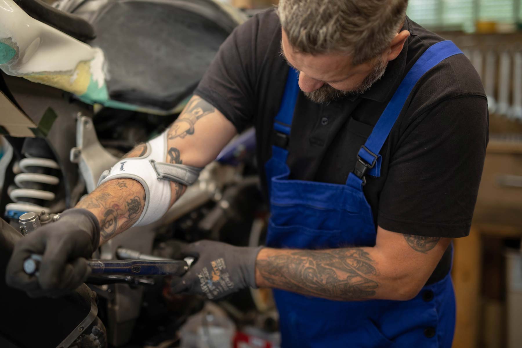 Mechanic repairs motorcycle and wears blue overalls and Masalo cuff against tennis elbow